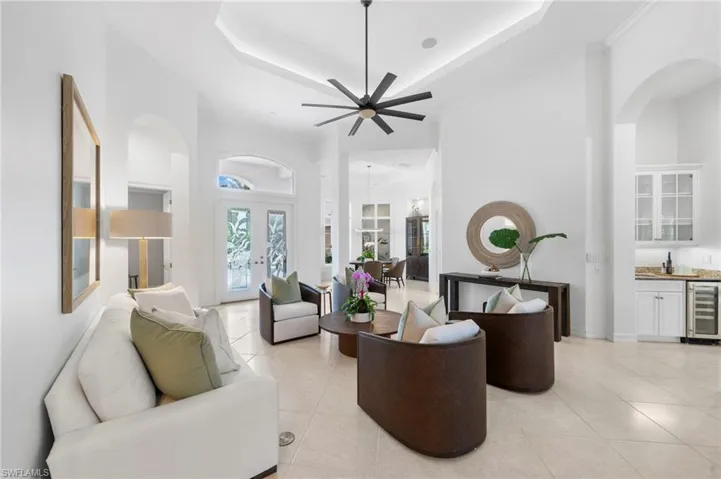 Tiled living room with french doors, ornamental molding, a raised ceiling, beverage cooler, and ceiling fan