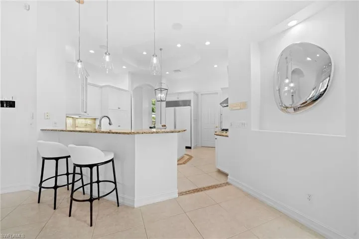 Kitchen with hanging light fixtures, white cabinetry, light stone countertops, light tile patterned flooring, and kitchen peninsula