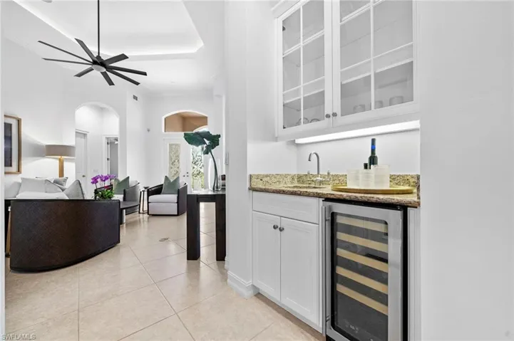 Bar with sink, beverage cooler, light tile patterned floors, light stone counters, and white cabinets