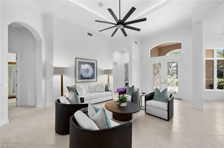 Tiled living room featuring ceiling fan, a towering ceiling, ornamental molding, and french doors