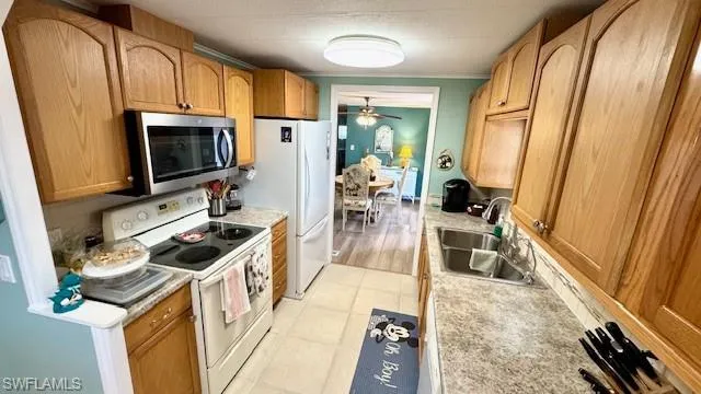Kitchen with white appliances, sink, ceiling fan, light wood-type flooring, and ornamental molding