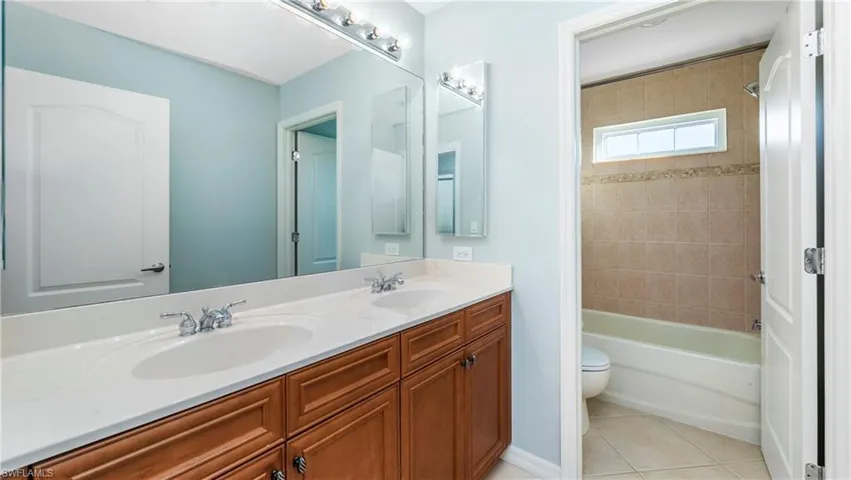Bathroom with double vanity, light tile patterned flooring, and washtub / shower combination