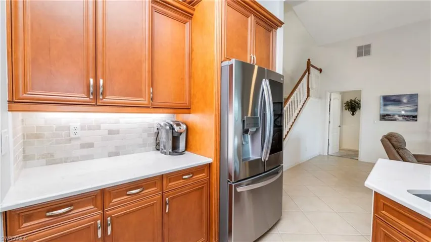 Kitchen featuring stainless steel refrigerator with ice dispenser, wood finish cabinets, light stone countertops, light tile patterned floors, and backsplash