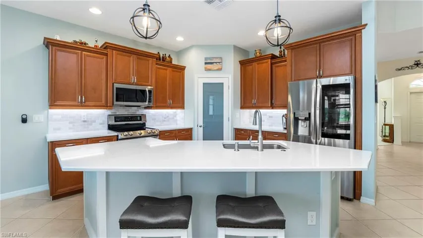 Kitchen with light tile patterned floors, arched walkways, a center island with sink, tasteful backsplash, and stainless steel appliances