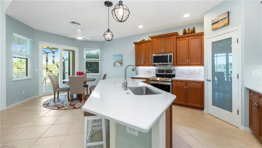 Kitchen featuring wood finish cabinetry, a center island with sink, stainless steel appliances, backsplash, and decorative light fixtures