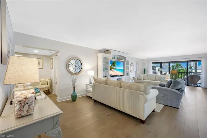 Spacious living area featuring light wood-finish flooring, a built-in media console with shelving, and an expansive glass slider opening to a balcony