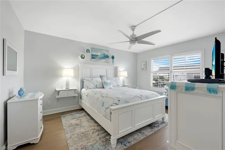 Light wood-finish flooring with a ceiling fan, dual windows featuring plantation shutters, and recessed wall shelving