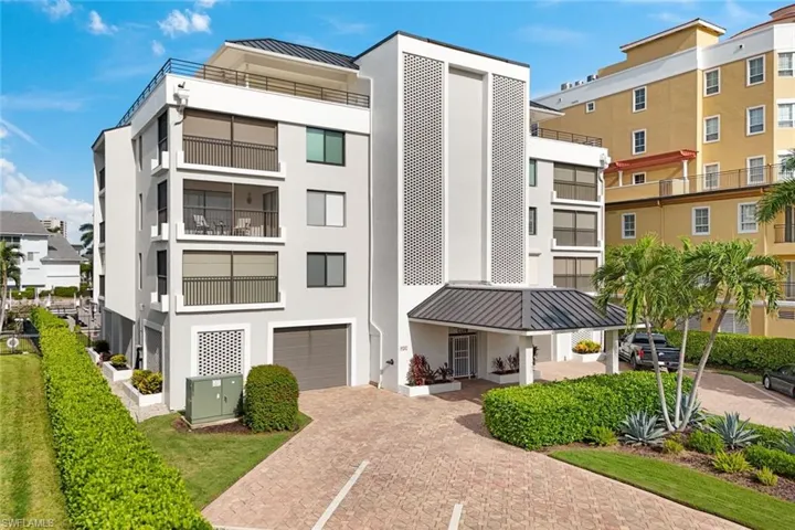 Multi-story building with multiple balconies, a rooftop terrace, an awning-covered entrance, and a paver driveway