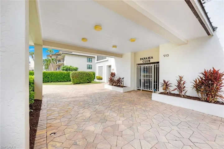 Covered entry featuring a geometric paver driveway, recessed lighting, and integrated landscaping with mature plantings