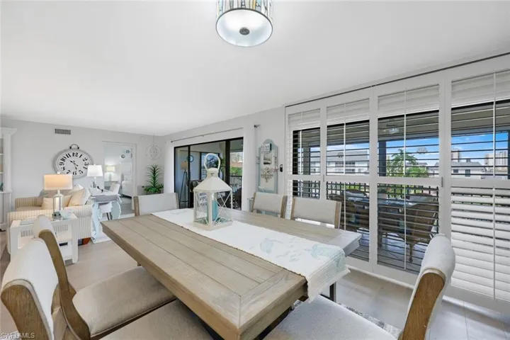 Dining area with wood-finish flooring, a contemporary ceiling light fixture, and white plantation shutters on a sliding glass door