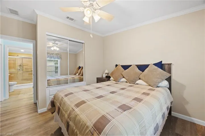 Bedroom featuring wood-finish flooring, crown molding, a ceiling fan with integrated lighting, and a closet with sliding mirrored doors