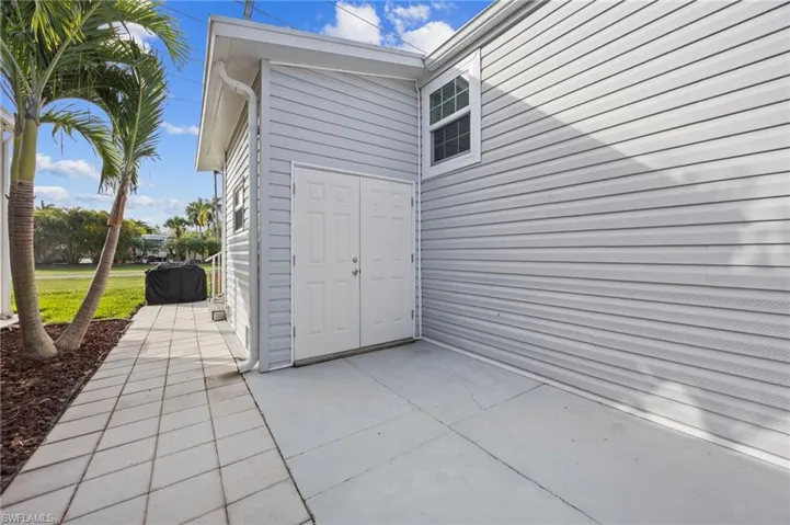 Exterior featuring light gray horizontal siding, a concrete patio, double-door entry, and a paved walkway