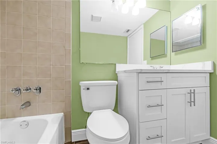 Bathroom featuring a white vanity with a white countertop, chrome fixtures, a full-width mirror, and tiled bath surround