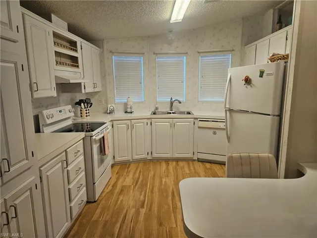 Kitchen with white appliances, wallpapered walls, light countertops, light wood finished floors, and a textured ceiling
