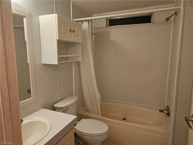 Bathroom with shower / tub combo, vanity, a textured ceiling, and wallpapered walls