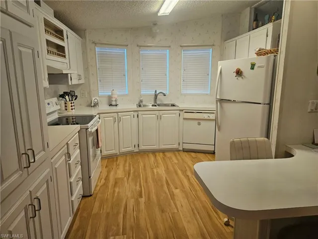 Kitchen featuring white appliances, light countertops, a textured ceiling, wallpapered walls, and white cabinets