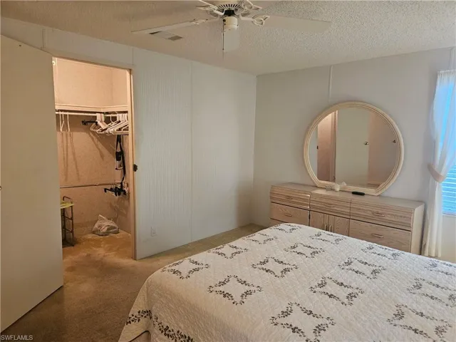 Carpeted bedroom featuring a walk in closet, ceiling fan, and a textured ceiling