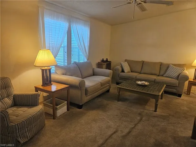 Living room with a textured ceiling, carpet flooring, and ceiling fan