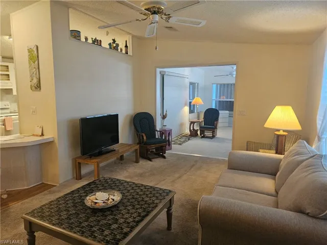 Living room with carpet floors, a textured ceiling, lofted ceiling, and a ceiling fan