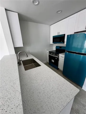 Contemporary kitchen featuring speckled countertops, white shaker cabinetry, stainless steel sink with gooseneck faucet, and integrated overhead lighting