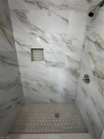 Shower featuring large-format wall tiles with a natural stone pattern and a hexagonal mosaic tile floor