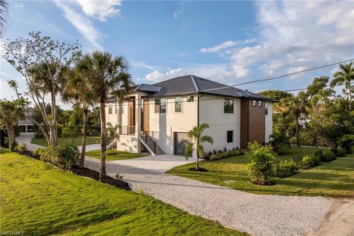 Contemporary home with driveway, a front yard, stucco siding, and a metal roof
