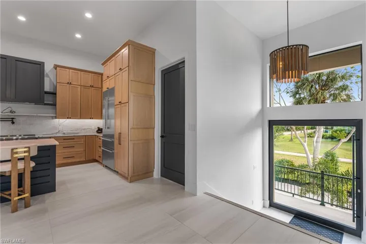 Kitchen with light brown cabinetry, hanging light fixtures, stainless steel built in refrigerator, backsplash, and recessed lighting