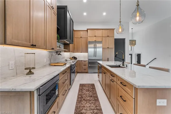 Kitchen featuring light stone counters, recessed lighting, built in appliances, a spacious island, and pendant lighting