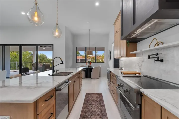 Kitchen featuring light stone countertops, appliances with stainless steel finishes, wall chimney range hood, hanging light fixtures, and recessed lighting