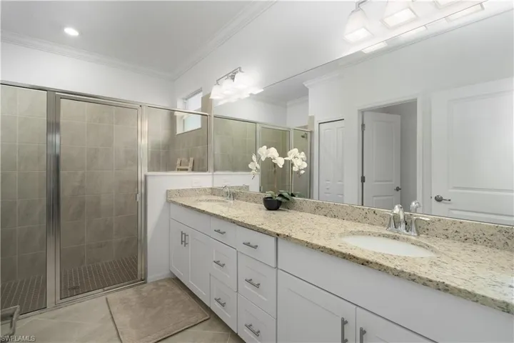 Primary bathroom with dual sinks, large tile shower and crown molding