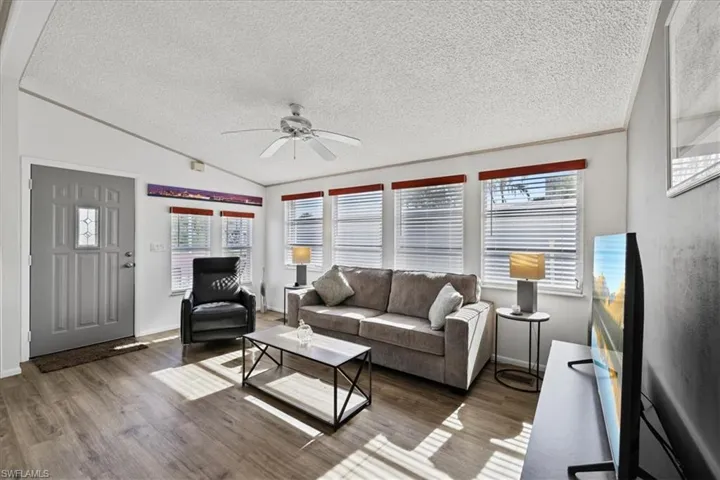 Living area with wood finished floors, lofted ceiling, a textured ceiling, ceiling fan, and crown molding