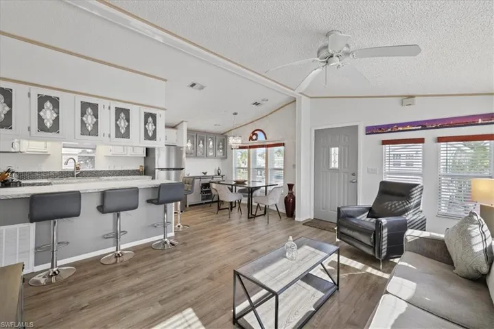 Living room featuring lofted ceiling, light wood-style floors, a textured ceiling, and ceiling fan