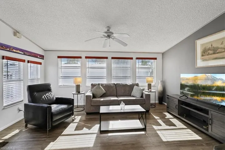 Living area with ornamental molding, a textured ceiling, a ceiling fan, and dark wood-style flooring