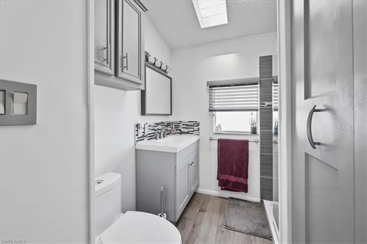 Full bathroom with a skylight, vanity, a textured ceiling, light wood-style floors, and backsplash