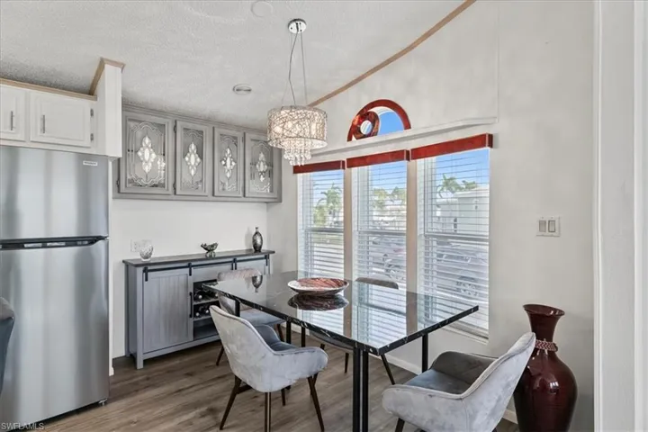 Dining area featuring dark wood-style flooring, a textured ceiling, a chandelier, ornamental molding, and vaulted ceiling