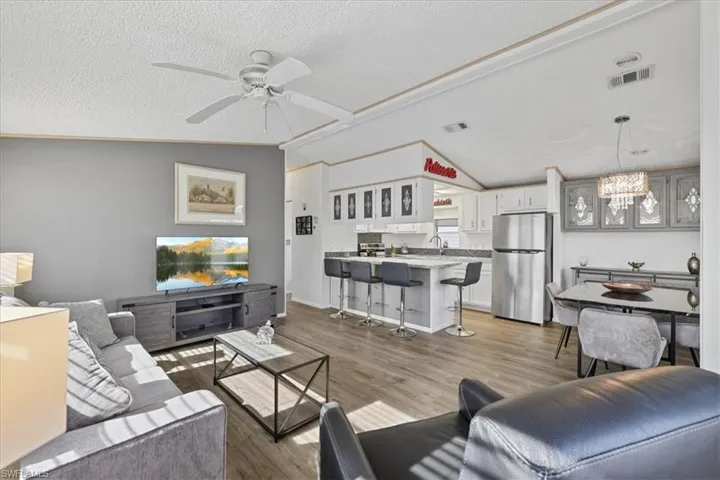 Living room with lofted ceiling, wood finished floors, a textured ceiling, a chandelier, and a ceiling fan