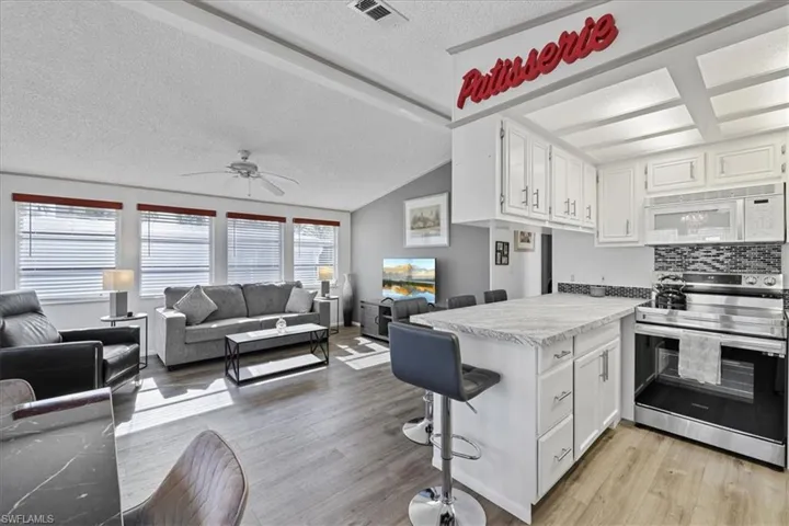 Kitchen featuring white cabinets, stainless steel range with electric stovetop, vaulted ceiling, a textured ceiling, and a peninsula