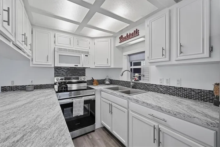 Kitchen featuring electric range, white cabinets, white microwave, light wood finished floors, and backsplash
