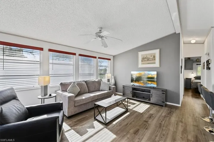 Living room featuring vaulted ceiling, a textured ceiling, wood finished floors, and a ceiling fan