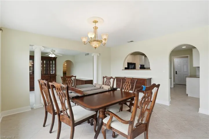 Dining area with arched walkways, hanging lights, a ceiling fan, and light tile patterned floors
