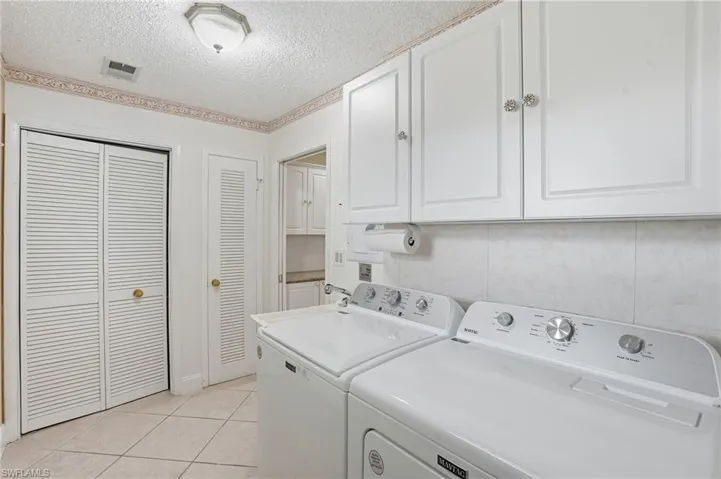 Laundry room with cabinet space, a textured ceiling, light tile patterned floors, and washing machine and dryer