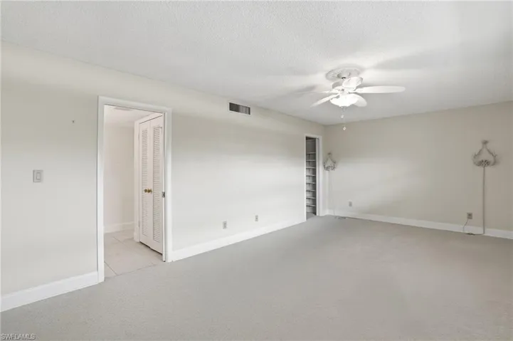 Empty room with light colored carpet, ceiling fan, and a textured ceiling