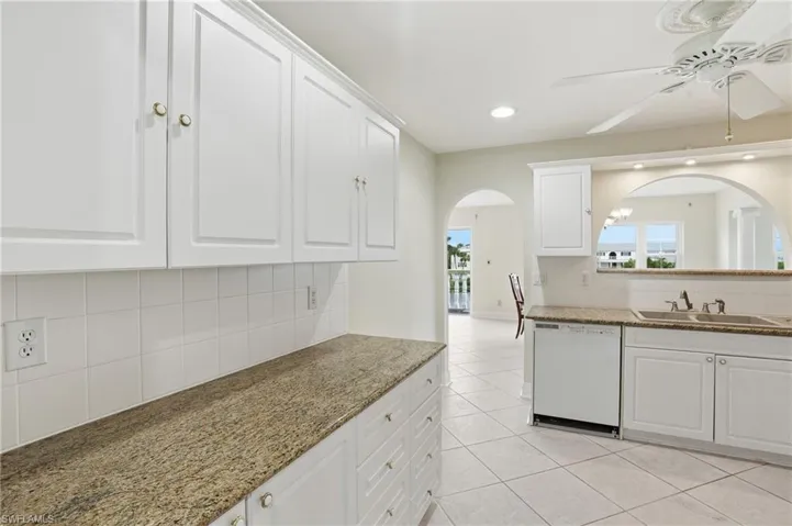 Kitchen featuring tasteful backsplash, white cabinetry, ceiling fan, white dishwasher, and light stone countertops