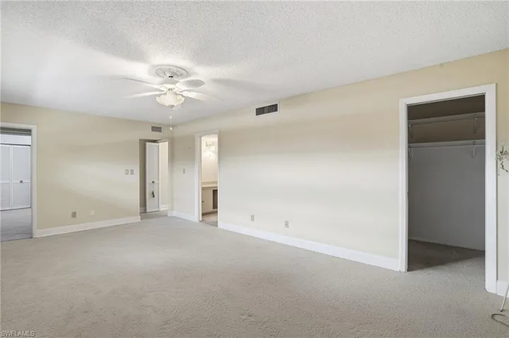 Unfurnished bedroom with carpet, a walk in closet, a textured ceiling, and a ceiling fan