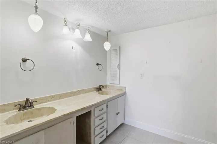 Full bath with double vanity, light tile patterned floors, and a textured ceiling