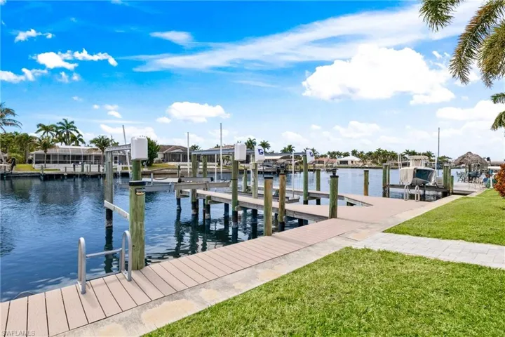 Dock area with boat lift, a water view, and a lawn