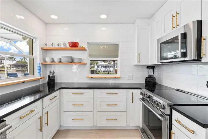 Kitchen with stainless steel appliances, dark stone counters, open shelves, white cabinetry, and decorative backsplash