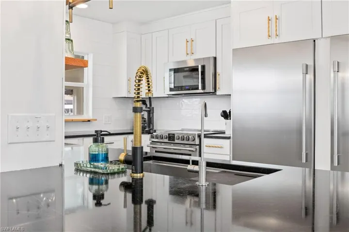 Kitchen featuring stainless steel appliances, white cabinets, backsplash, and dark stone countertops
