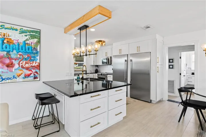 Kitchen with stainless steel appliances, a kitchen bar, white cabinets, hanging light fixtures, and a peninsula
