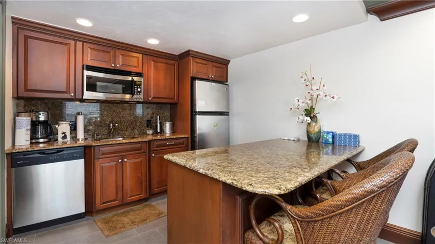 Kitchen featuring a kitchen bar, decorative backsplash, stainless steel appliances, light stone counters, and a peninsula